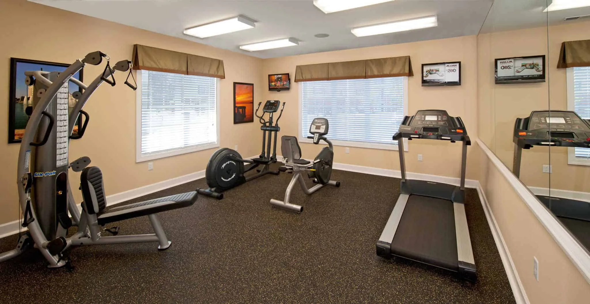 A bright community fitness center equipped with a treadmill, elliptical, stationary bike, and a multi-station weight machine