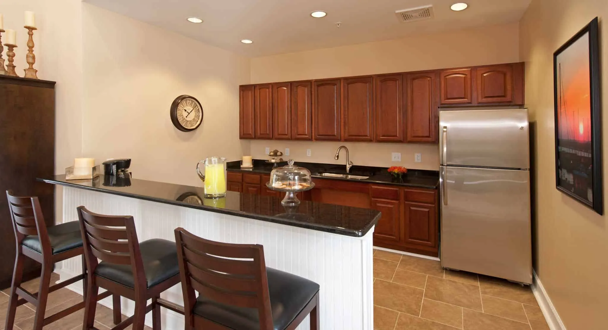 A modern clubhouse kitchen and bar area featuring dark wood cabinetry, black granite countertops, stainless steel appliances, and leather barstools A modern clubhouse kitchen and bar area featuring dark wood cabinetry, black granite countertops, stainless steel appliances, and leather barstools