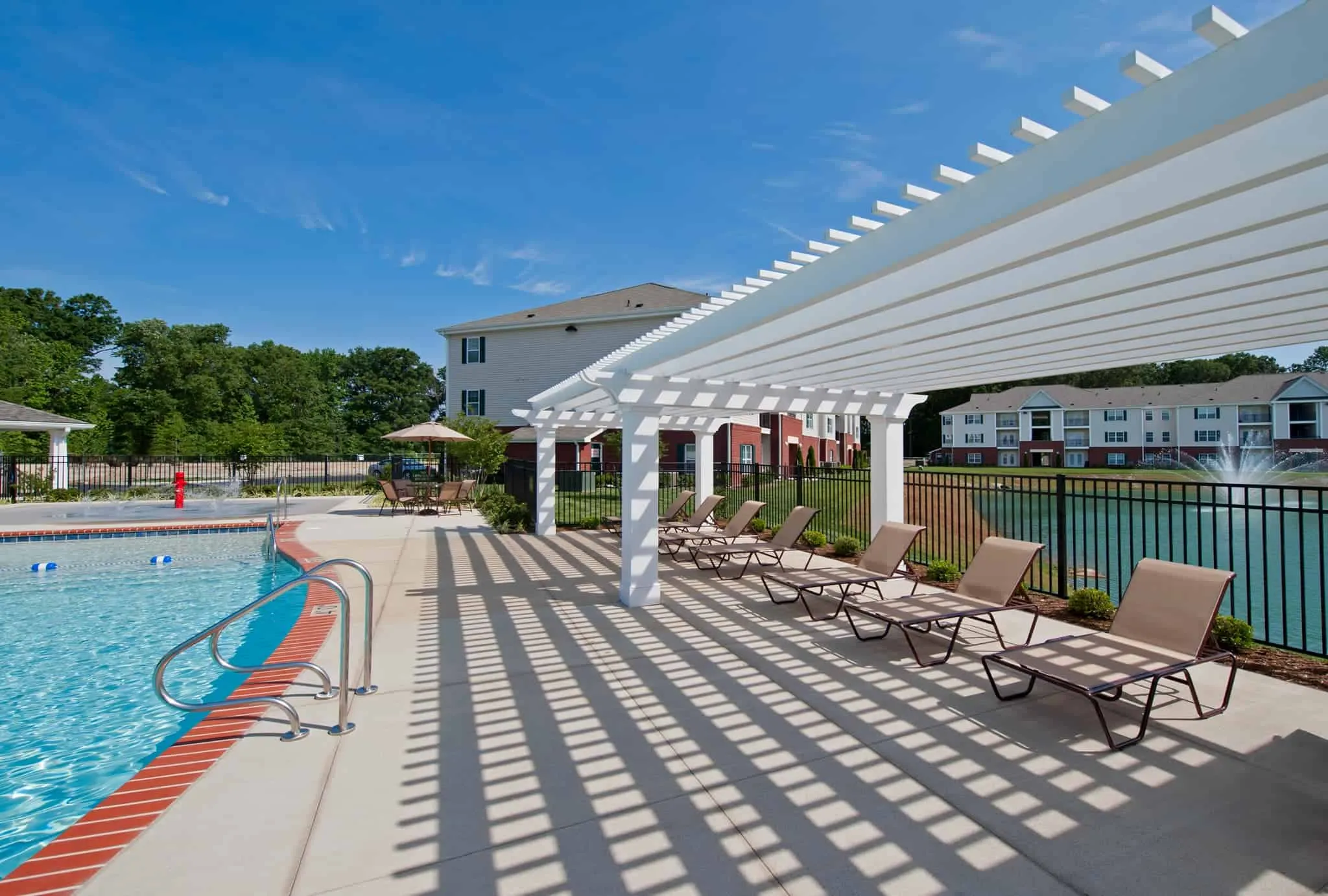 A sun-drenched pool deck featuring several lounge chairs positioned under the shade of a white pergola